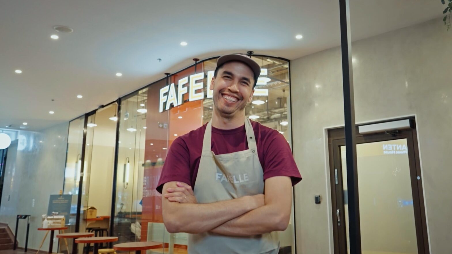 En man med stort leende, som står med armarna i kors framför sin restaurang.